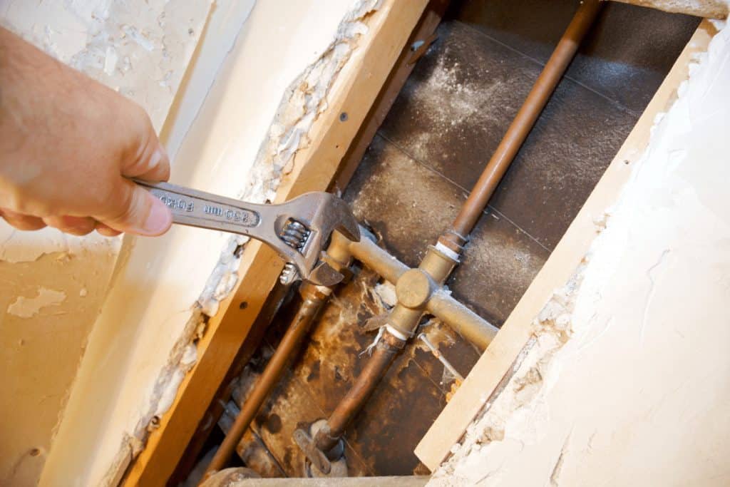 Worker from Pipeworks Plumbing and Construction uses a wrench to adjust copper pipes within an exposed wooden wall frame, demonstrating professional plumbing installation during residential construction.