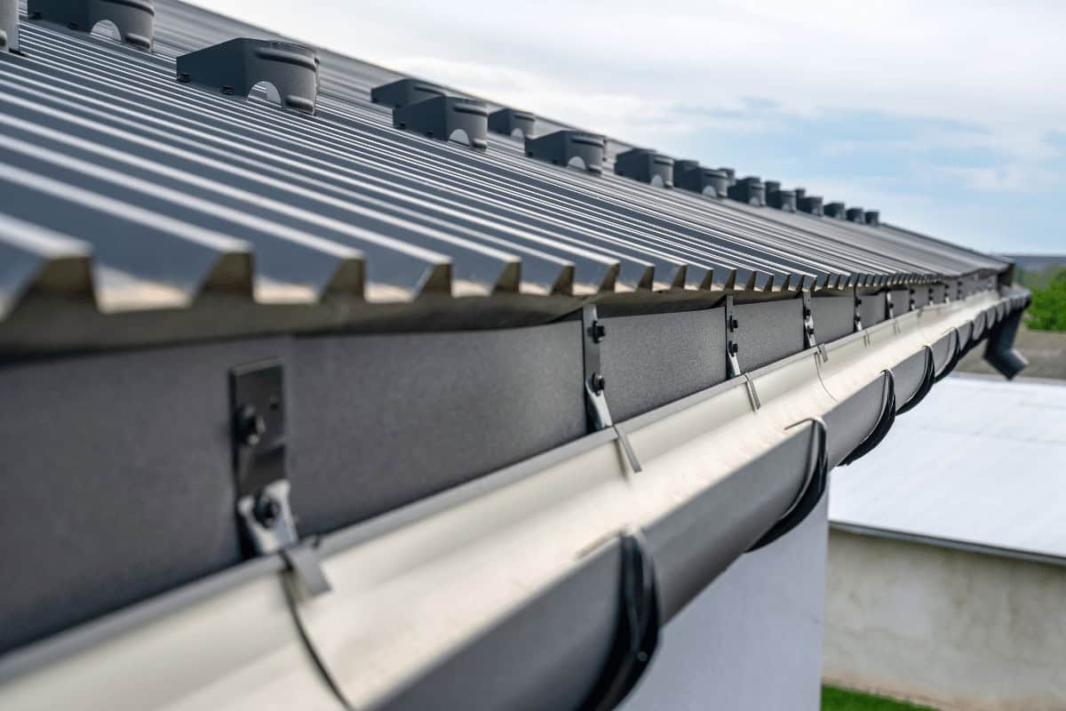 Close-up of a modern metal roof with dark gray panels and matching gutters installed by Pipeworks Plumbing and Construction on a residential home, showcasing professional roofing, secure fastenings, and expertly integrated plumbing under a partly cloudy sky.