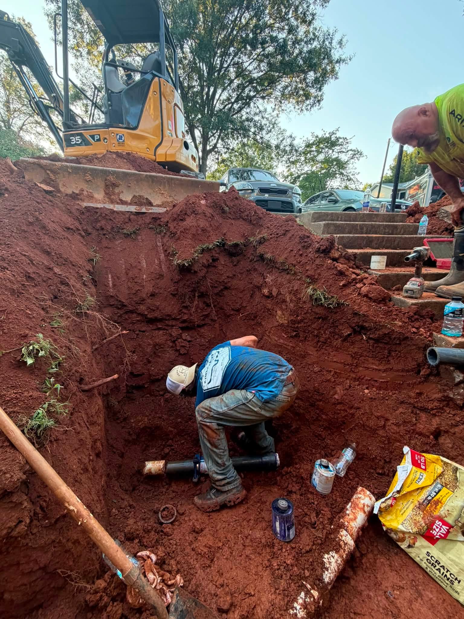 Two Pipeworks crew members joining water pipe in an excavation beside concrete steps with solvent cement and fittings to hand