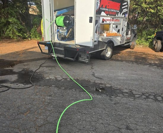 A Pipeworks Plumbing and Construction service trailer equipped with green plumbing hoses and professional tools is parked on cracked asphalt near trees; a hose extends from the trailer, showcasing the company’s branding and pipework construction expertise.