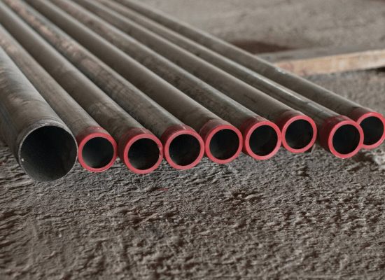 Eight metal pipes with red end caps, arranged in a row on a rough concrete floor, showcasing plumbing materials used by Pipeworks Plumbing and Construction—side view highlights circular pipe openings typical for basement drain backup inspections. Eight metal pipes with red end caps, arranged in a row on a rough concrete floor, showcasing plumbing materials used by Pipeworks Plumbing and Construction—side view highlights circular pipe openings typical for basement drain backup inspections.