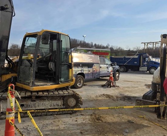 A Pipeworks Plumbing and Construction job site showing a yellow excavator digging near orange safety cones and caution tape—potentially for sewer line repair or plumbing installation—with a blue dump truck and service van parked nearby under a clear sky.