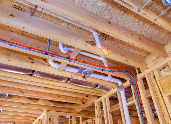 Exposed wooden ceiling framing in a building under construction, featuring white PVC plumbing pipes, blue and red water supply lines, electrical wiring, and insulation installed by Pipeworks Plumbing and Construction. Essential commercial pipework installation in progress. Exposed wooden ceiling framing in a building under construction, featuring white PVC plumbing pipes, blue and red water supply lines, electrical wiring, and insulation installed by Pipeworks Plumbing and Construction. Essential commercial pipework installation in progress.